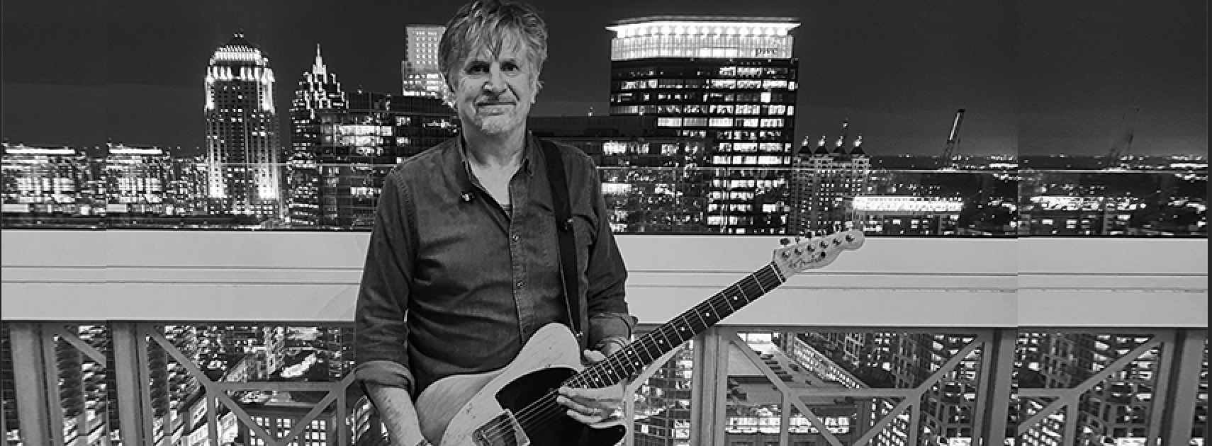 Mike McLeod with guitar in front of the Atlanta skyline at night